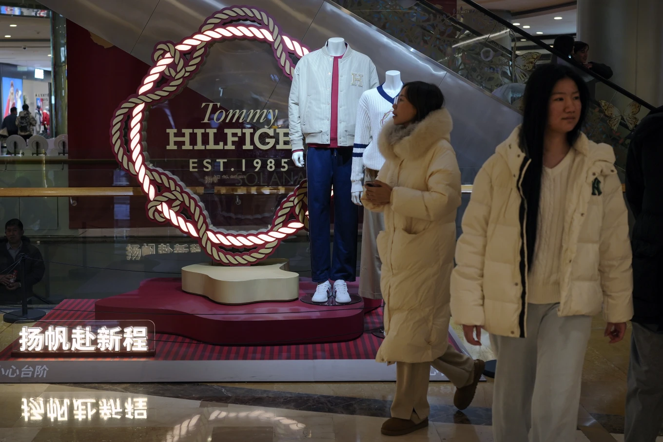 Women walk by a fashion display of Tommy Hilfiger, which is owned by PVH Group, at a shopping mall in Beijing