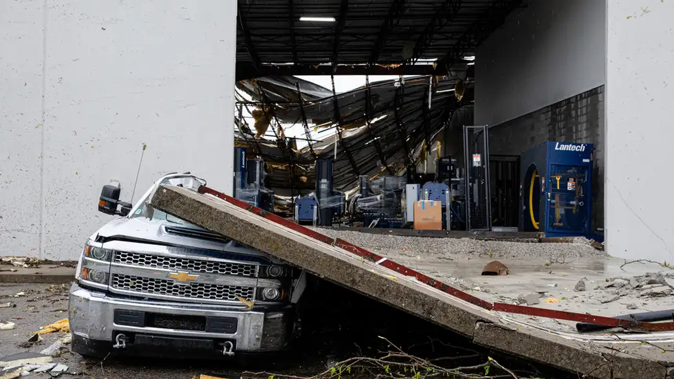 A smashed truck sits under a section of collapsed warehouse wall after violent storms and tornadoes tore through the area